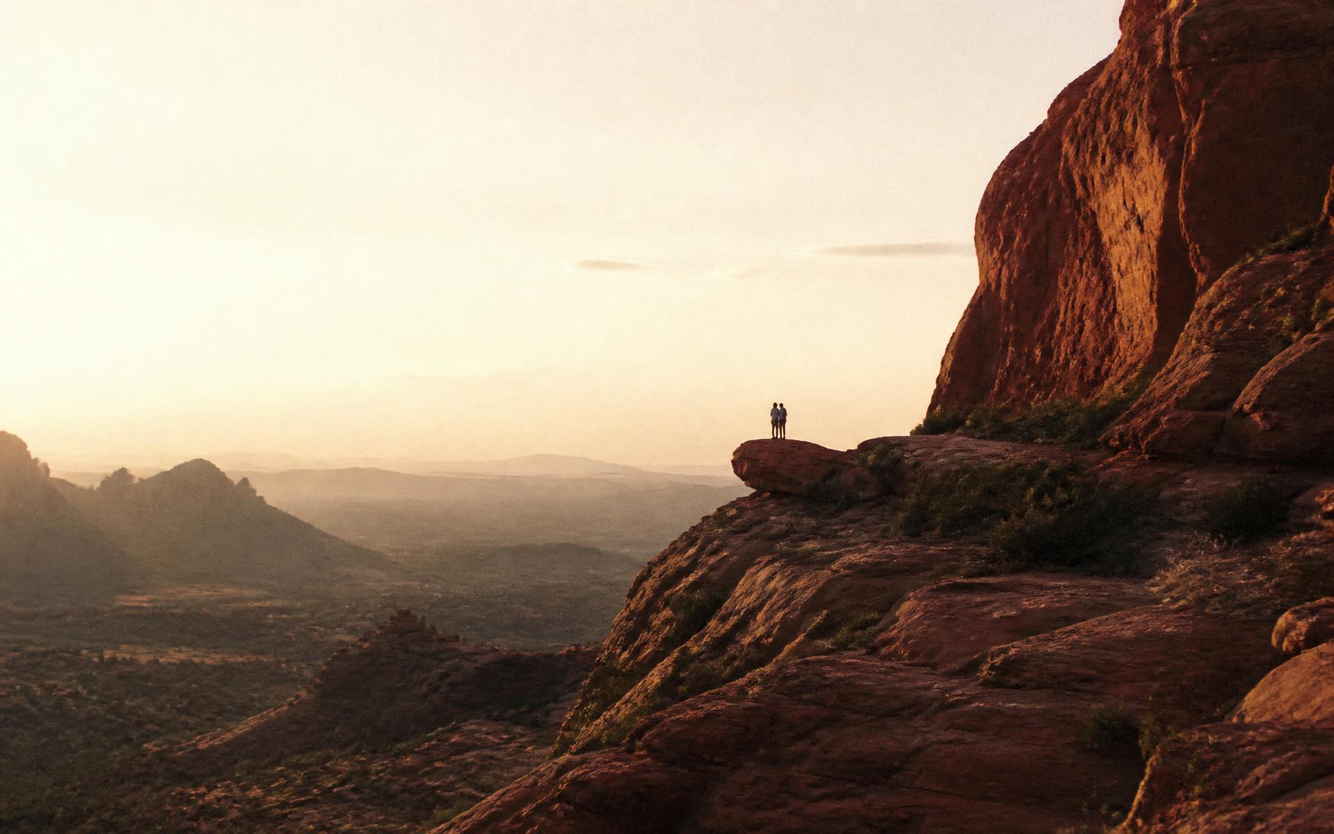 A couple standing on a red rock ledge above the Sedona valley at golden hour